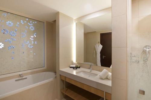La salle de bains est pourvue d'une baignoire, d'un lavabo et d'un miroir. dans l'établissement Hilton Taghazout Bay Beach Resort & Spa, à Taghazout