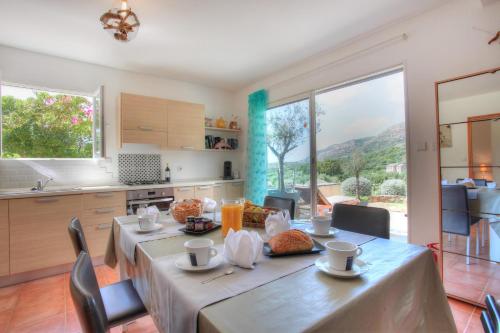 d'une salle à manger avec une table et d'une cuisine avec de grandes fenêtres. dans l'établissement Les Oliviers CENTURI-PORT, à Centuri