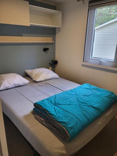 a bed with a blue comforter and a window at Mobilhome 6 à 8 personnes camping 4 etoiles in Saint-Cyprien