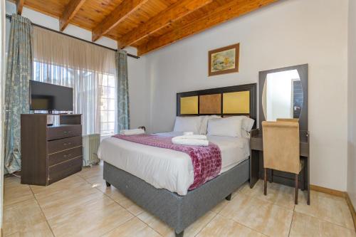Dormitorio con cama, escritorio y TV en Royal Olympia Lodges & Safaris RSA, en Sandton