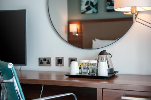 a desk with a mirror and a table with a lamp at Hilton Garden Inn London Heathrow Airport in Hillingdon