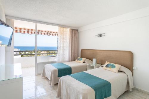 two beds in a room with a view of the ocean at Apartamentos Borinquen in Playa de las Americas