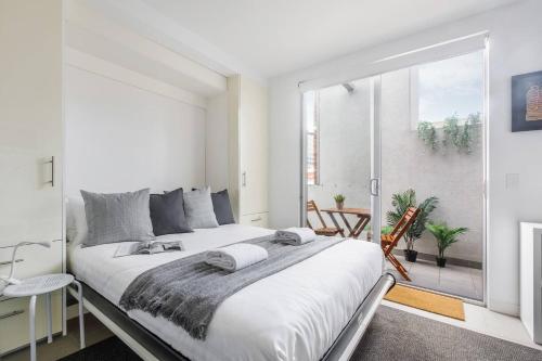 a white bedroom with a large bed and a window at Nicholson's Nest - A Balcony Studio in Funky Fitzroy in Melbourne