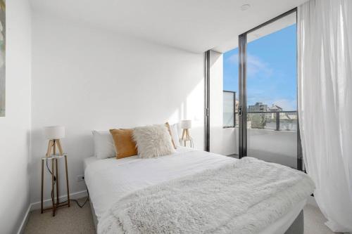 a white bedroom with a bed and a large window at The Nest on Nott - Pure Port Melbourne Bliss in Melbourne