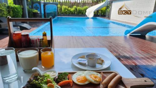 a breakfast tray with eggs and vegetables on a table next to a pool at Sky dome resotel - โรงแรมสกายโดม รีโซเทล in Bangkok