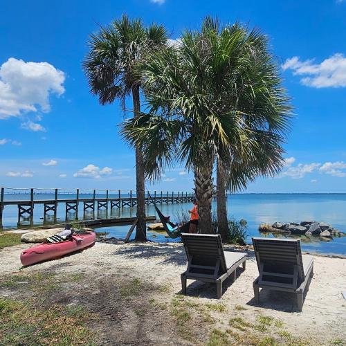 a beach with two chairs and two palm trees at Nasa waterfront Dolphin Suite in Titusville