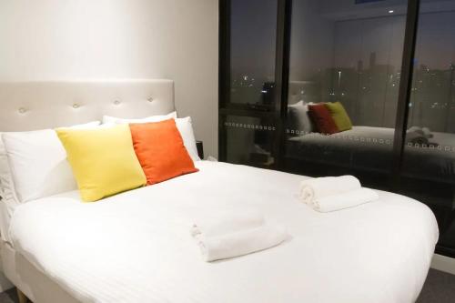 a white bed with two colorful pillows on it at Modern Spacious 2BD2Bath - Stunning City Views! in Melbourne
