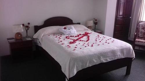 a bed with red rose petals on it at Coraza Hotel in Otavalo