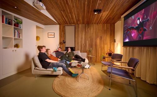 Hoteldebootel 's-Hertogenbosch met prive sauna في سيرتوخيمبوس: مجموعة من الناس يجلسون في غرفة المعيشة ويشاهدون التلفزيون