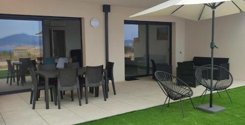 un patio avec une table, des chaises et un parasol dans l'établissement T3 neuf, vue mer, à Pietrosella