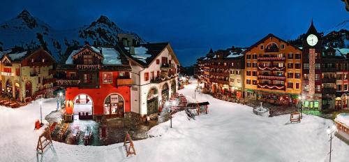a group of buildings in the snow with a clock at Résidence Pierre & Vacances Premium Arc 1950 Le Village in Arc 1950