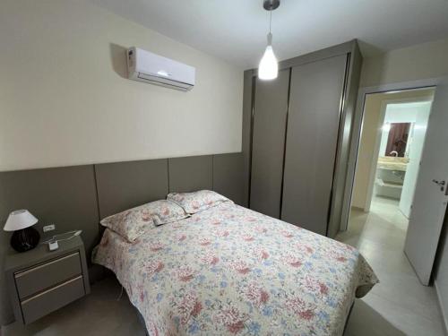 1 dormitorio con 1 cama con colcha de flores y mesita de noche en Apartamento Manchester, en Bombinhas