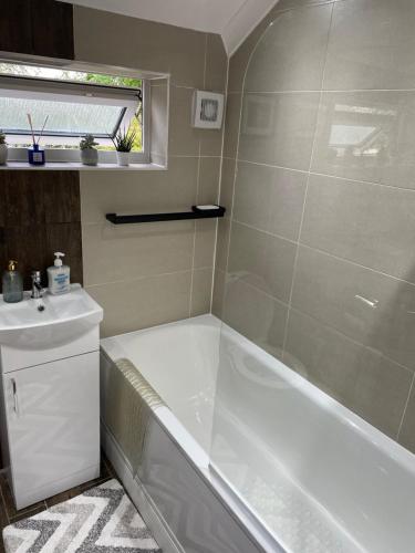 a bathroom with a tub and a sink at Lovely 4 bed house with patio & bbq in Slades Green