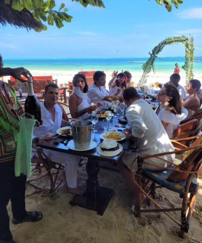 a group of people sitting at a table on the beach at Sipano Beach Lodge Kiwengwa in Kiwengwa