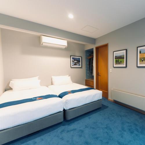 two beds in a room with blue carpet at The Box House in Furano
