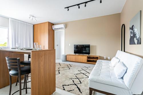 a living room with a white couch and a kitchen at Prédio com apartamentos completos, com piscina e a passos da praia - Agua Marinha in Florianópolis