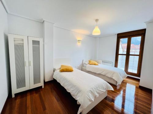 2 Betten in einem Zimmer mit weißen Wänden und Holzböden in der Unterkunft Excelente apartamento con garaje y piscina in Ramales de la Victoria