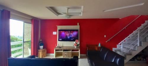 Casa com Belas vistas - Muriqui في مانغاراتيبا: غرفة معيشة مع جدار احمر مع تلفزيون بشاشة مسطحة
