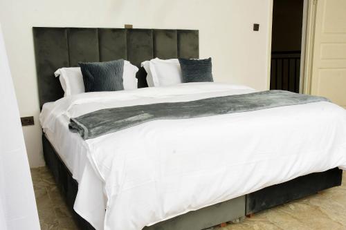 uma cama grande com lençóis brancos e almofadas em Deluxe and Standard en-suite rooms at The White House em Eldoret