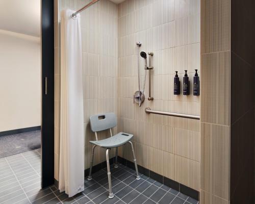 a shower with a chair and a shower curtain at Aloft Leawood-Overland Park in Overland Park