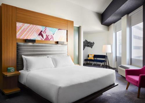 a bedroom with a white bed and a pink chair at Aloft Leawood-Overland Park in Overland Park