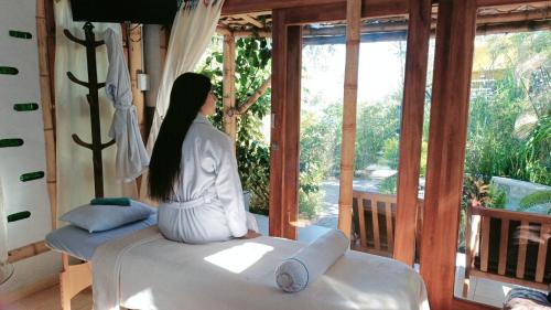 a woman sitting on a bed looking out of a window at Hostería Colibri Aeropuerto in Tababela