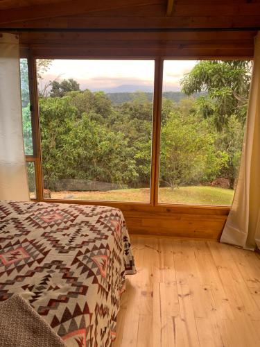 a bedroom with a bed and a large window at Las Nubes Cabaña in La Mesa