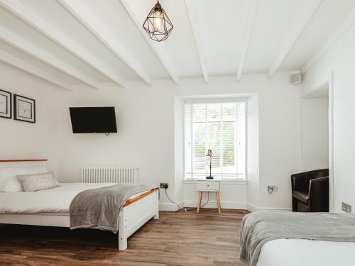 a white bedroom with two beds and a tv at Holmbyre Smithy in Dalry