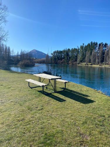 a picnic table and benches next to a river at Riverside Studio in Wanaka