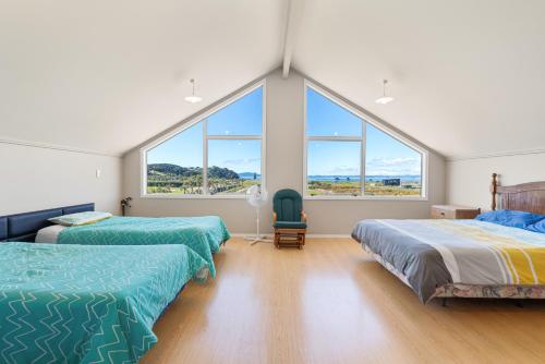 two beds in a room with large windows at Tokerau Magic - Karikari Peninsula Holiday Home in Kaitaia