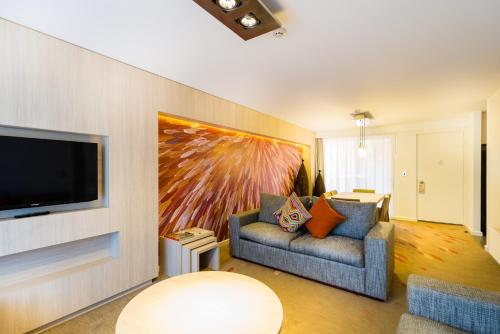 a living room with a couch and a tv on a wall at Emu Walk Apartments in Ayers Rock