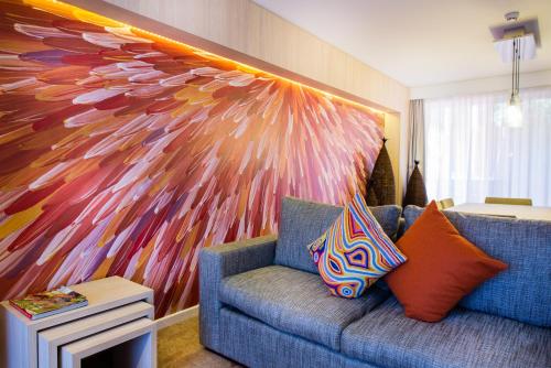 a living room with a blue couch and a colorful painting at Emu Walk Apartments in Ayers Rock