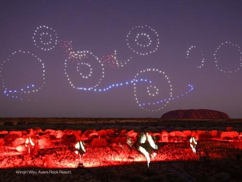 Un groupe de gens dansant autour d'un feu la nuit dans l'établissement Emu Walk Apartments, à Uluru
