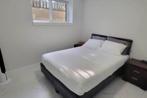 a bedroom with a bed with white sheets and a window at Lucy's Place - Two Bedroom Suite in Vancouver