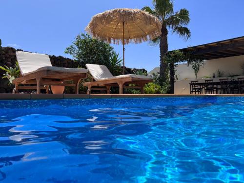 a swimming pool with chairs and an umbrella at Surf&fun heated pool villa in La Oliva