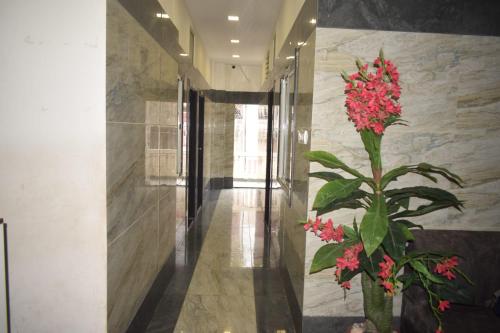 a hallway with a plant with red flowers in a vase at Hotel Lakshya Sheesh Mahal Indore in Indore