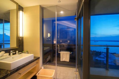 Holiday Inn Haikou West Coast, an IHG Hotel في هايكو: حمام مع حوض ودش زجاجي