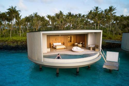 a house on the water with a boat in the water at The Ritz-Carlton Maldives, Fari Islands in North Male Atoll