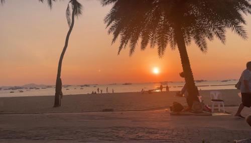 um pôr do sol na praia com palmeiras em Kann Villa Jomtien Beach & Yahaha em Praia de Jomtien
