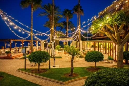 a courtyard with palm trees and lights at night at Hotel Los Ángeles Denia in Denia