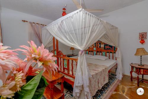 a bedroom with a canopy bed with white curtains and flowers at Suite Two Rooms - Watamu in Watamu