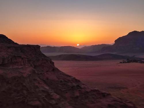 a sunset in the desert with mountains in the background at Desert Nights Camp in Wadi Rum