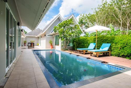 een zwembad in de achtertuin van een huis met blauwe stoelen en een parasol bij Colorful Pool Villa in Ban Chin Tham Mai