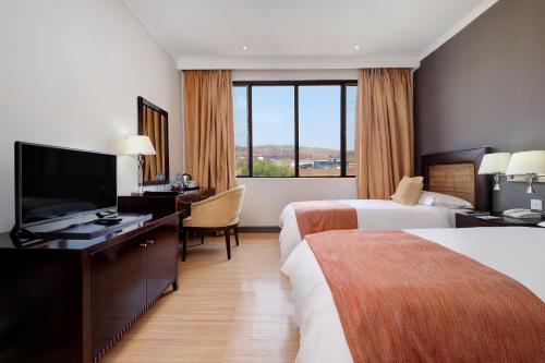 a hotel room with two beds and a desk and a television at Protea Hotel by Marriott Chipata in Chipata