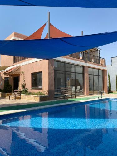 a pool in front of a building with a blue canopy at Jar AlQamar Chalet -شاليه جار القمر in Jerash