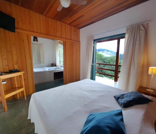 a bedroom with a bed and a bathroom with a window at Pousada Vale das Araucárias in Santo Antônio do Pinhal
