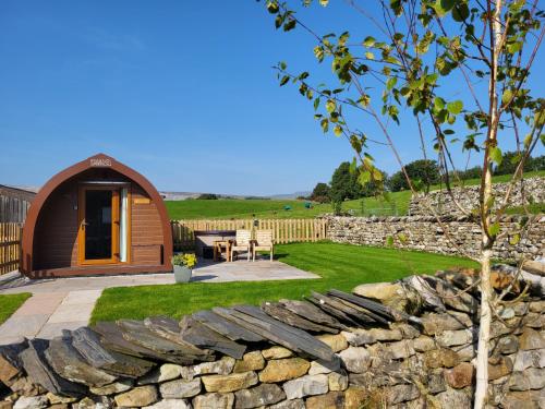 a garden with a wooden cabin and a stone wall at Ribblesdale Pods in Horton in Ribblesdale