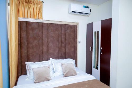 イケジャにあるGOD'S TOUCH APARTMENTS SHORT-LET Adenugba Street Oregun Ikeja Lagos Nigeriaのベッド(白い枕、茶色のヘッドボード付)