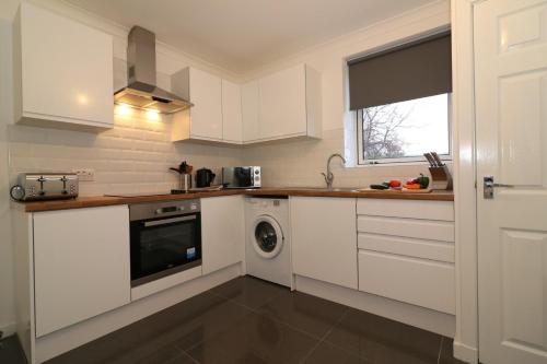 een keuken met witte kasten en een wasmachine bij Signature - Carrick View in Cumbernauld