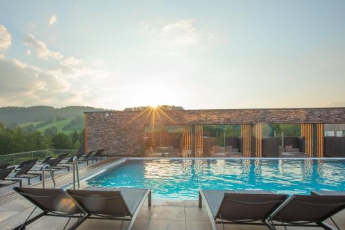 a large swimming pool with chairs and the sun setting at Familotel Schreinerhof in Schönberg